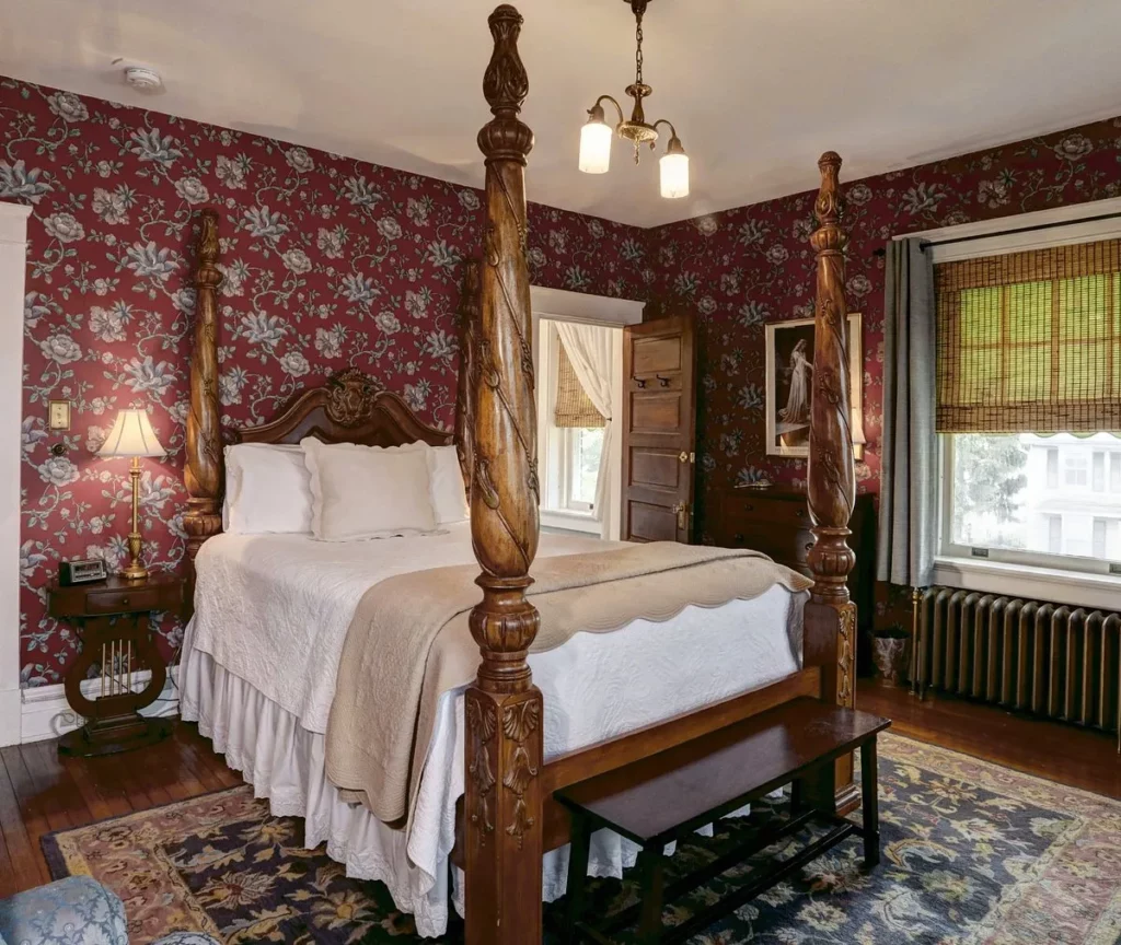 A cozy and elegant room at Olde Square Inn Bed and Breakfast with a queen-sized plantation-style bed and magnolia wallpaper.